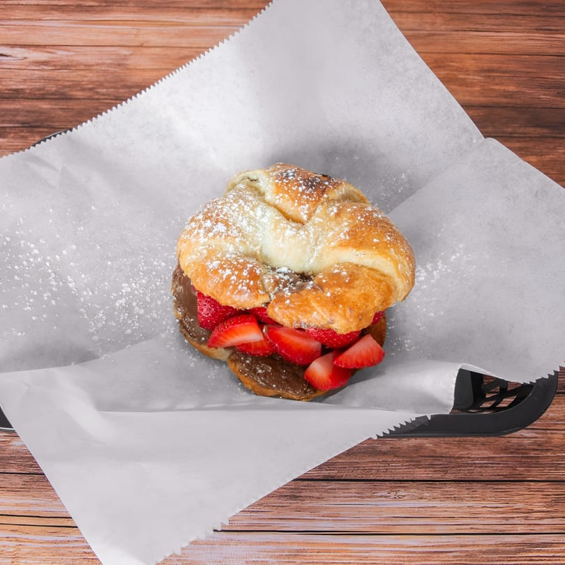 Croissant filled with chocolate spread and sliced strawberries, dusted with powdered sugar.