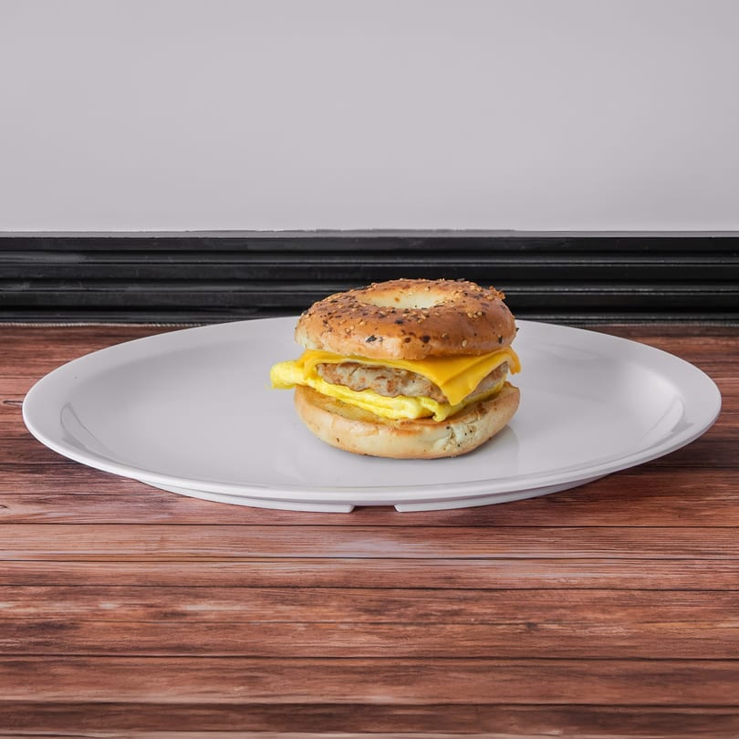 Breakfast sandwich with sausage, egg, and cheese on a sesame bagel, on a white plate.