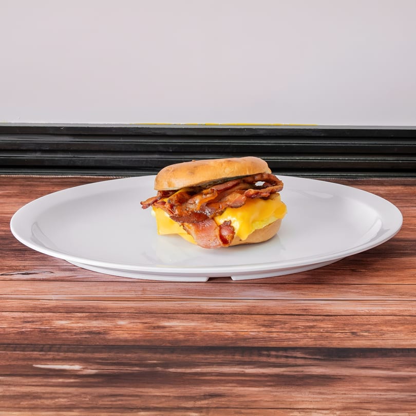 A bagel sandwich with bacon, egg, and melted cheese on a white plate.